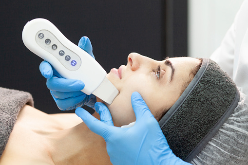procedure of ultrasonic cavitation facial peeling. facial skin care in a cosmetology clinic, a female cosmetologist makes facial cleaning to a client with a modern device