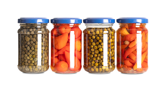 Pickled spices in small glass jars. From left to right capers, hot red baby peppers, green peppercorns, and piri piri chilis. Pasteurized and preserved in a brine of water, vinegar and salt. Photo.
