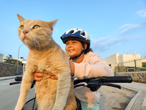 Close-up image of a Nine-year-old girl riding her bicycle with her cute domestic cat.