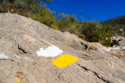 Striped lines in yellow and white painted on a rock, orientation sign to hikers.