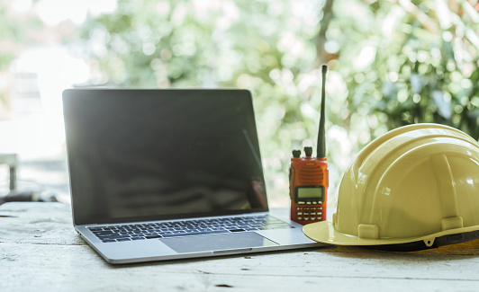 workspace with laptop, a hard hat on a wooden surface, likely belonging to a professional on a construction or engineering site.