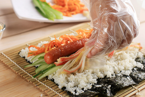 Close Up Korean Female Making Gimbap, Korean Roll Rice with Sausace, Kyuri, Carrot, and Crabstick. Step by Step Preparation Cooking