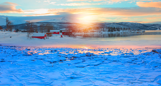 Beautiful winter landscape with red house and red cabin - Arctic city of Tromso - Breaking blue ice over frozen at sunrise - Norwegian Sea, Norway