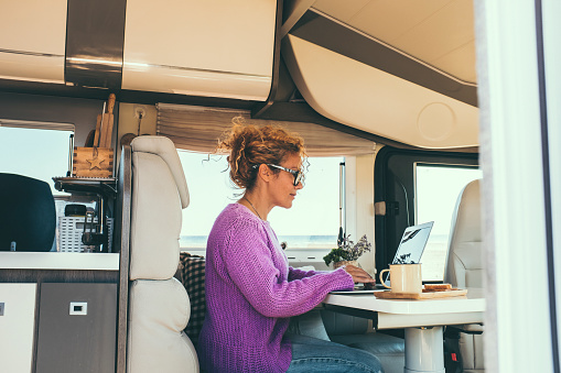 Woman works and plans sitting inside the camper. Concept of work and leisure on vacation