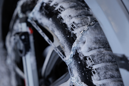 close up view from up close of snow chains mounted on a car wheel, partially frozen and covered by the snow, in winter