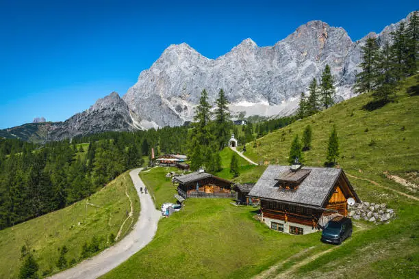 Famous hiking and travel location, rural wooden houses on the alpine green meadows. Picturesque Dachstein mountains in background, Ramsau am Dachstein, Styria, Europe