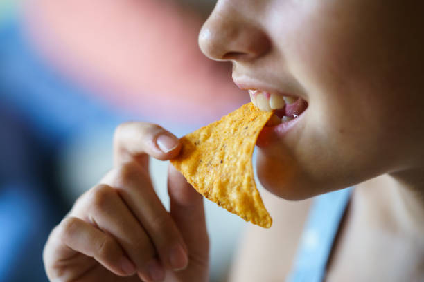 Unrecognizable happy teenage girl biting spicy nacho chip at home stock photo