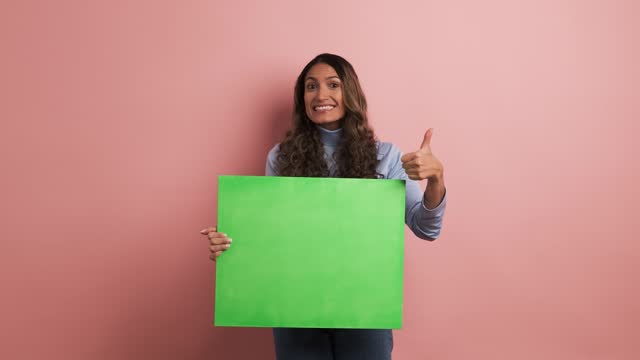 Smiling woman holding a green board and gesturing thumb up