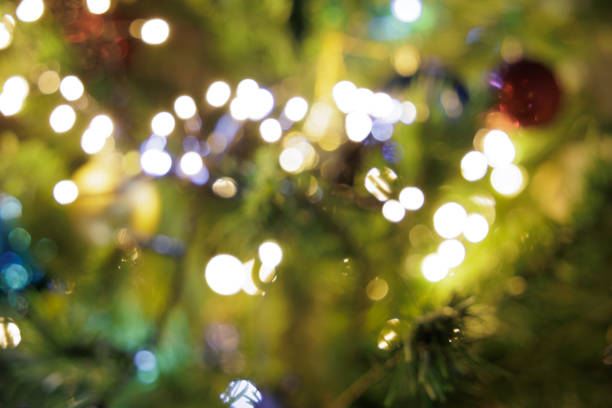 close up view showing a blurred Christmas tree, decorated with small bright lights and various colorful decorations