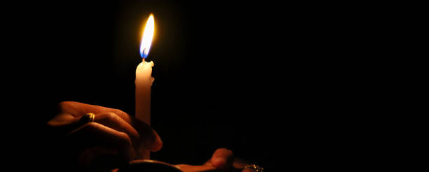 Hands holding a burning candle in the darkness