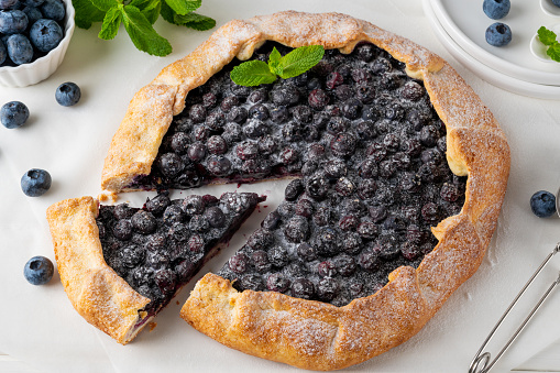 Blueberry galette, open pie or tart with ice cream and cup of tea on a white wooden table. Summer sweet pie