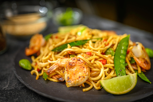 Spaghetti with prawns and vegetables on black table.