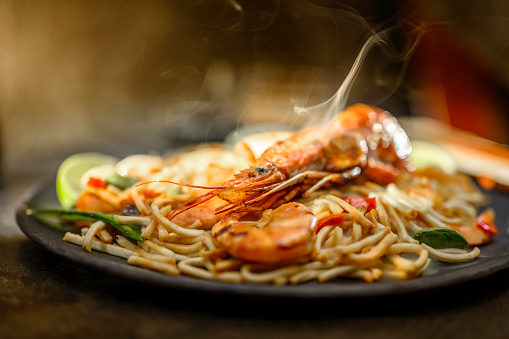 Spaghetti with prawns and vegetables on black table.