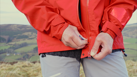 Female hiker having problems with the zipper on her rainjacket.