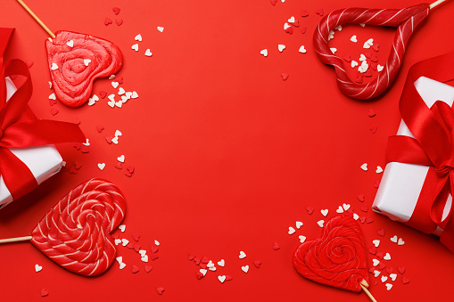 Heart lollipops: Sweet treats and gift boxes on a red backdrop with text space. Flat lay Valentines day card