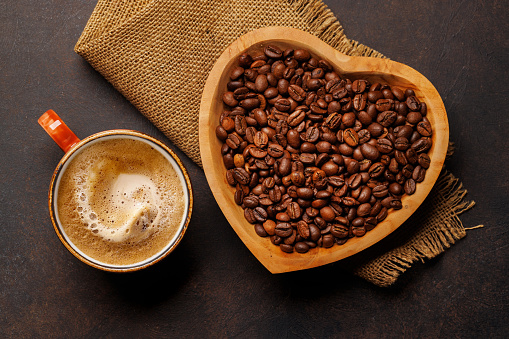 Coffee love: A cup and heart-shaped bowl with roasted beans. Flat lay