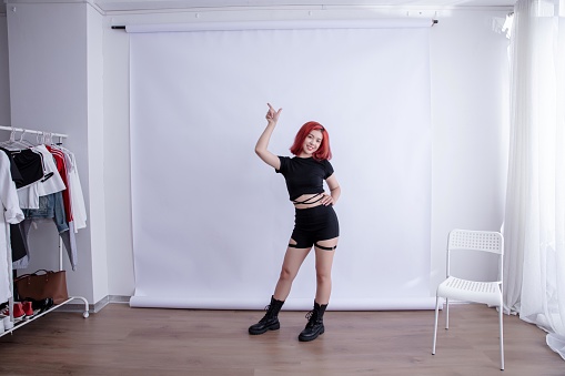 Asian woman in black outfit dancing in front of white background,