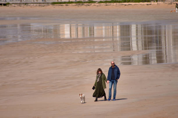 Couple walking on a cold but sunny day in March along Playa América in Nigrán accompanied by dogs