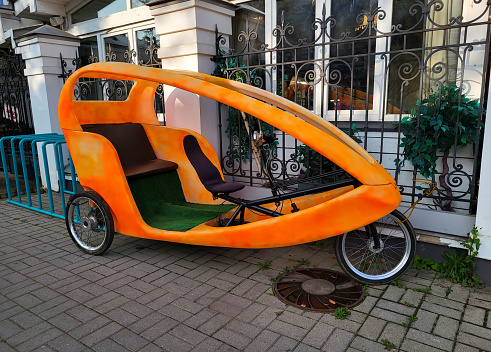 Three-wheeled transport, an orange bicycle pole stands near the fence on the sidewalk