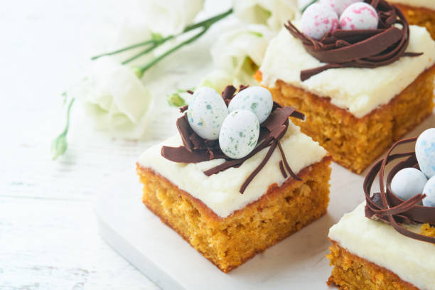 istock Easter carrot cake bars decorated with chocolate nest and chocolate candy eggs blossoming cherry or apple flowers on rustic light wooden backgrounds. Easter holiday meal. Traditional Easter food. 1914876535