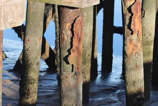 Close up of legs of a rusty pier standing on sand