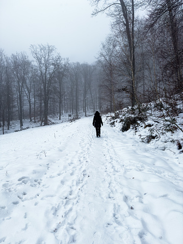 A woman is enjoying a walk in the freshly snow-covered forest and is crossing a small clearing.