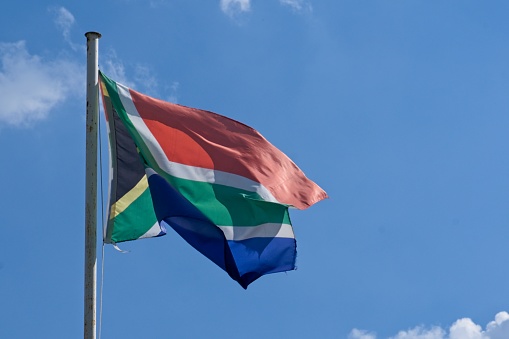 Close up of South African flag on flagpole blowing in the breeze with blue sky background