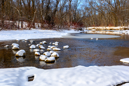 Snow covered rocks in a shallow river bed with ice and open water