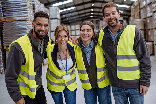 Full team of warehouse employees standing in warehouse. Team of workers in reflective clothing in modern industrial factory, heavy industry, manufactrury. Group portrait.