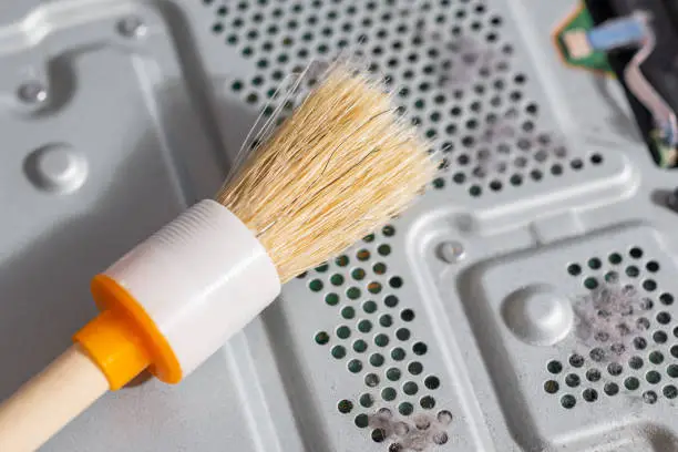 Photo of Cleaning the computer parts from dust using a brush. Dusty ventilation holes in the air cooling system