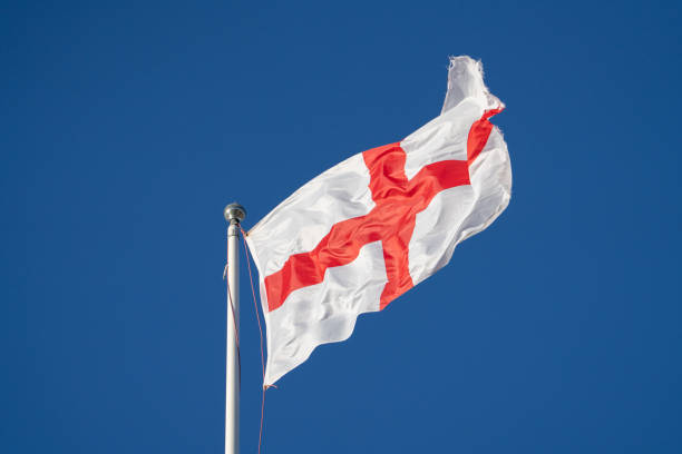 drapeau de l’angleterre sur le poteau battant dans l’aile contre le ciel bleu - english flag st george flag flying photos et images de collection