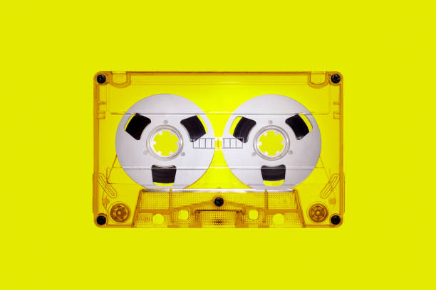 istock Clear plastic retro audio cassette with spools, isolated on yellow background in close up. The picture is intended for design work on the theme of music 1915069931