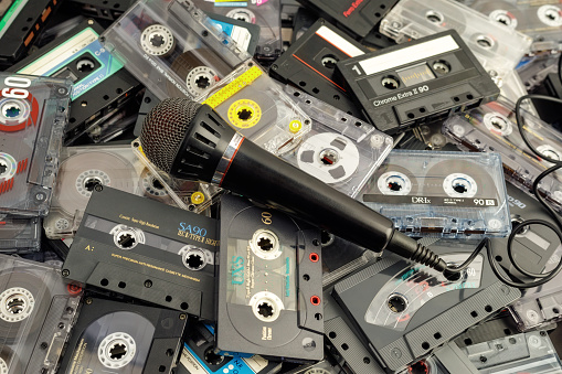 A pile of vintage audio cassettes scattered in disarray. A background of different, colorful audio media and a microphone on them.