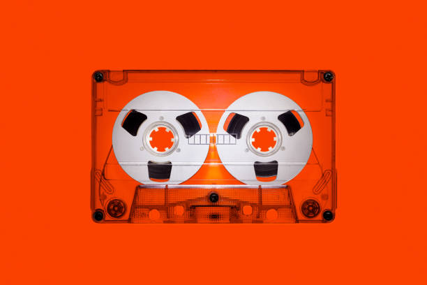istock Clear plastic retro audio cassette with spools, isolated on orange background in close up. The picture is intended for design work on the theme of music 1915070476