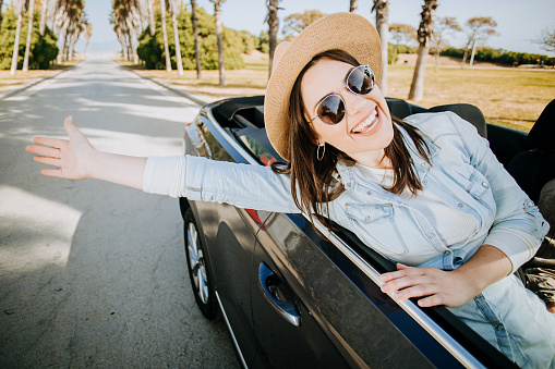 Happy young woman enjoying freedom on travel trip driving a cabriolet car on summer vacation