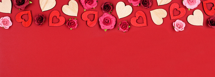 Valentines Day top border of wooden hearts and roses. Above view on a red banner background. Copy space.