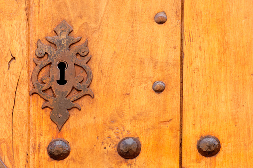 Traditional ancient wooden weathered  brown door, cast iron keyhole and old nails . Castrillo de los Polvazares, León, Castilla y León, Spain. Copy space on the left.