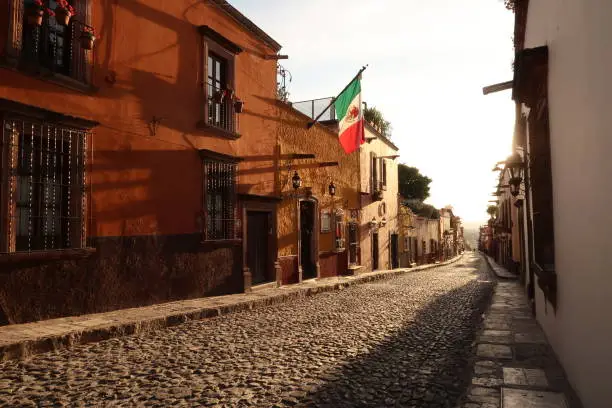 Photo of Typical cobblestone street in San Miguel de Allende at golden hour/sunset, a mexican flag is hanging on a facade, Mexico