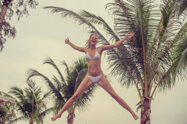 Beautiful young woman jumping at palms tree background stock photo