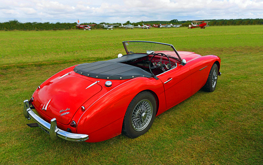 Little Gransden, Cambridgeshire, England - August 27, 2023:  Classic Red Austin Healey 3000 motor car parked on airstrip with aeroplanes in background