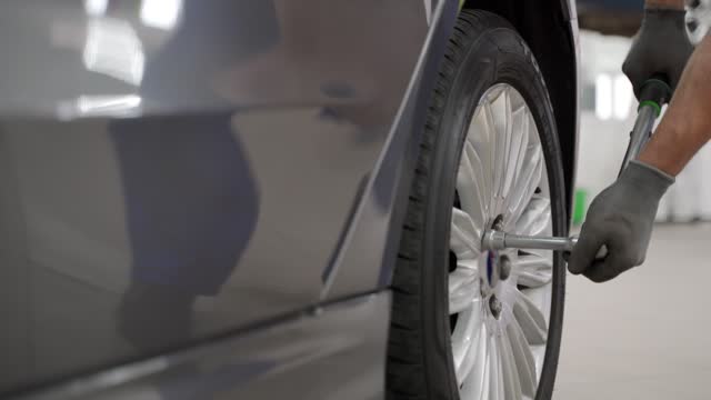 Auto mechanic attaches alloy wheel to luxury sedan using torque wrench in high-end garage. Professional, precise tire installation ensures safe, optimal vehicle performance. Expert secures rim.