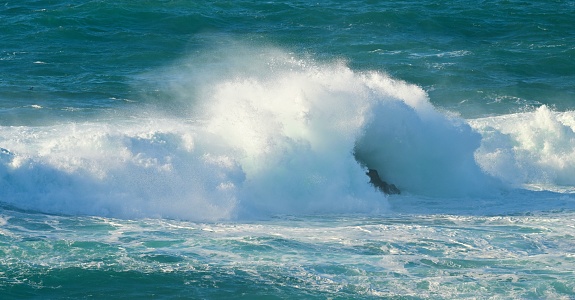 Ocean wave breaking on rock just offshore in Laguna Beach, California. White spray in the air;  blue sky in background.