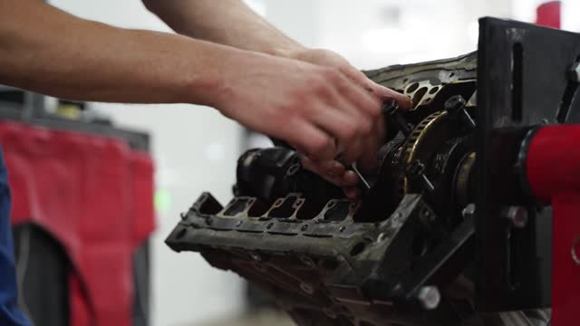 Auto mechanic disassembles engine block at service station. Expert removes crankshaft, bearings in repair shop. Vehicle maintenance, engine parts visible. Professional car overhaul caught on video.