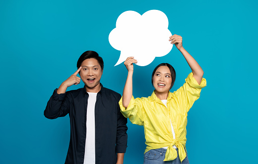 Positive young asian woman in casual hold abstract cloud with free space, man got idea, point finger at head, isolated on blue studio background. Think, brainstorm and dreams, create solution
