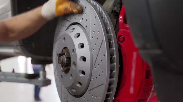 Auto mechanic installs new brake disc, caliper on vehicle. Car repair service procedure, maintenance workshop. Technician replaces brakes, pads, checks rotor. Garage safety inspection process.