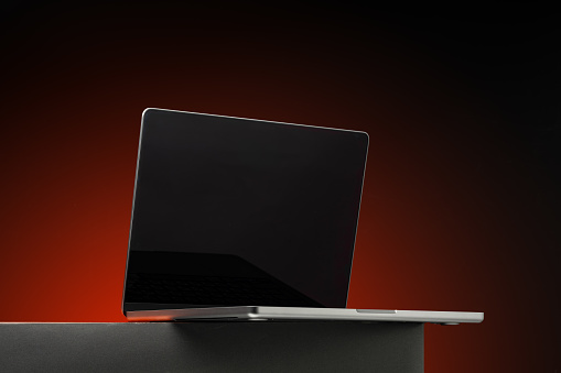 Laptop with black screen against dark red background close up