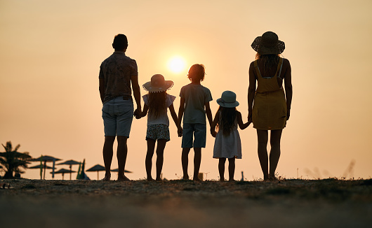 Family vacation holiday, Happy family running on the beach in the evening. Back view of a happy family on a tropical beach and a car on the side. Mother, father, children on the sea at sunset.