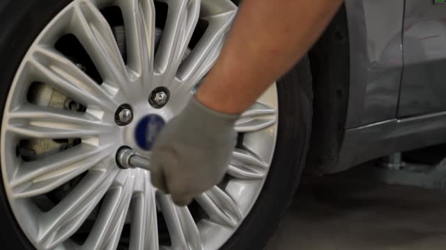 Auto mechanic secures tire on premium vehicle using torque wrench. Expert ensures wheel alignment, safety in high-end car service. Professional work, tire installation, precision maintenance.