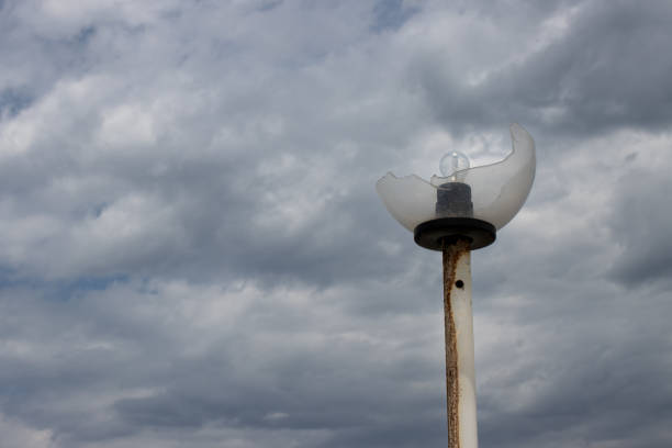 Old rusted lampost with a broken glass cover of the bulb, which is stil there. Intense cloudy sky. Roda, Corfu, Greece.