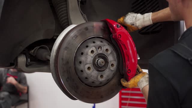 Auto mechanic installs new disc brake on car. Professional replaces brake pads in garage. Vehicle maintenance work, hands in gloves fixing brakes, caliper installation, auto repair service.
